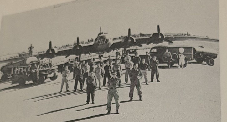 A row of B-17 Flying Fortress bombers with aircrew standing in front on an airfield apron